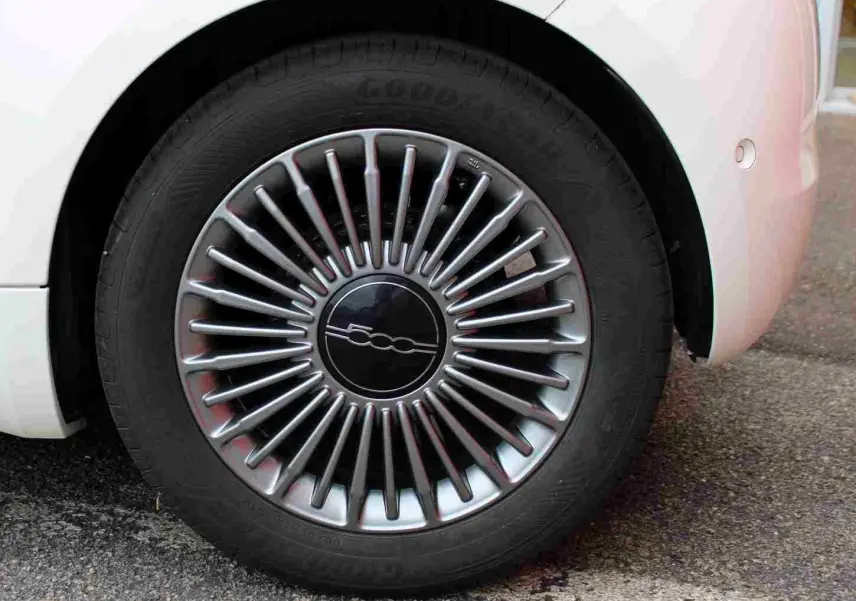 Gros plan sur la roue avant droite d'une FIAT 500 électrique blanche, avec jante multibranches argentée et logo central 500.