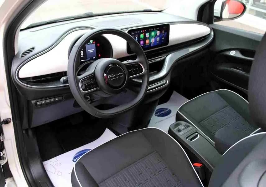 Intérieur de la FIAT 500 électrique 2023 vu côté conducteur, tableau de bord blanc et écran tactile avec CarPlay.