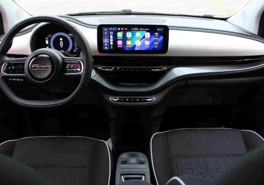 Vue intérieure frontale du tableau de bord de la Fiat 500 électrique blanche avec écran tactile et volant multifonction.