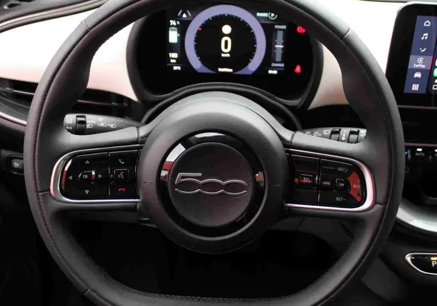 Vue rapprochée du volant noir de la Fiat 500 électrique 2023 avec tableau de bord numérique et écran tactile CarPlay.
