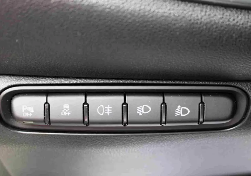 Gros plan sur les boutons de commande d’éclairage et d’aide à la conduite dans une Fiat 500 électrique blanche, intérieur noir.