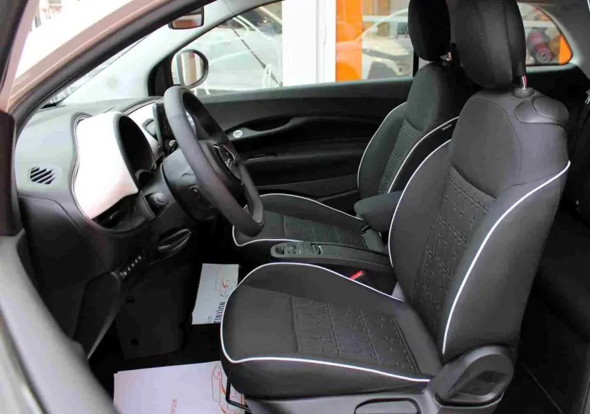 Vue intérieure côté gauche de la Fiat 500 électrique 2023, sièges noirs avec surpiqûres blanches et tableau de bord blanc.