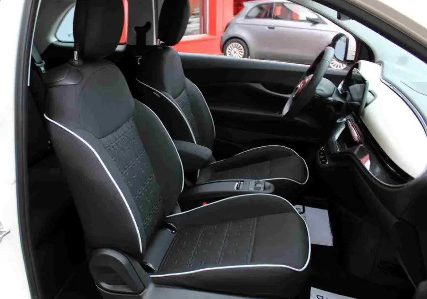 Vue intérieure côté gauche de la FIAT 500 électrique blanche 2023, montrant les sièges noirs avec surpiqûres blanches et le tableau de bord.