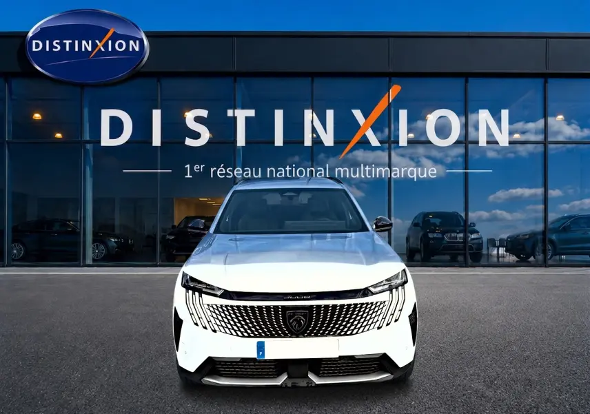 Vue frontale d'un Peugeot 5008 blanc garé devant une vitrine Distinxion avec calandre noire distinctive.