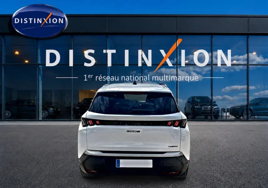 Vue arrière d’un Peugeot 5008 Hybrid blanc 2025 avec feux LED et lunette arrière surteintée devant une vitrine Distinxion.