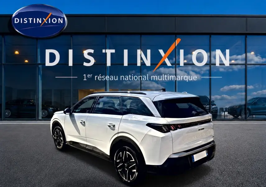 Peugeot 5008 blanc en 3/4 arrière droit, avec jantes alu noires et vitres arrière surteintées devant showroom Distinxion.
