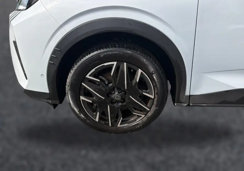 Gros plan sur la roue avant gauche avec jante alu noire et argentée du Peugeot 5008 blanc Hybrid 145 allure 2025.