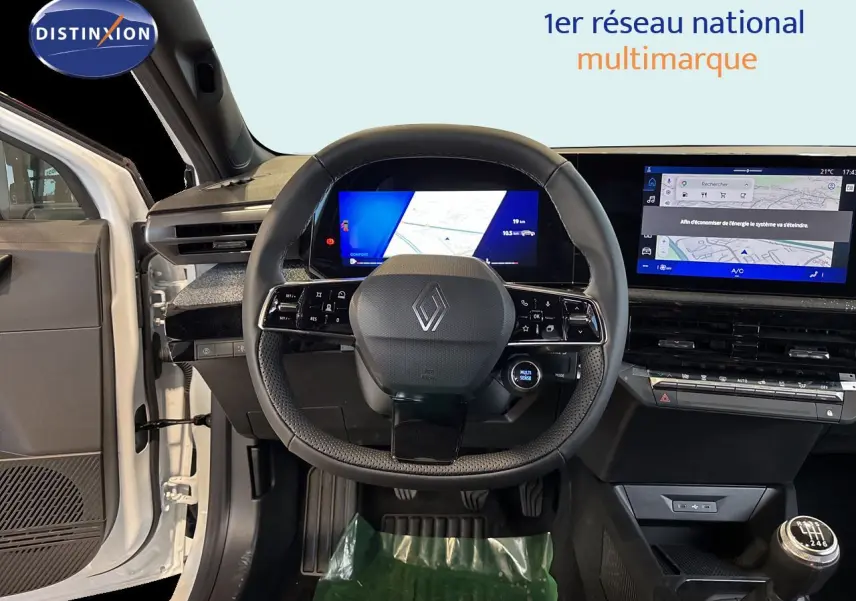 Vue intérieure centrée sur le volant Renault d’une Clio blanche 2026, avec tableau de bord numérique et boîte manuelle visible.