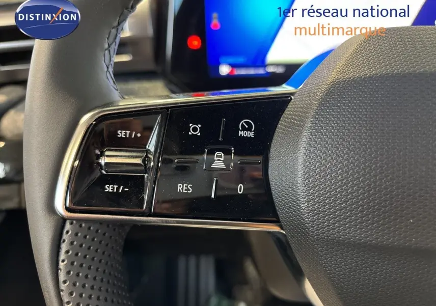 Gros plan sur les commandes à gauche du volant noir perforé de la Renault Clio VI TCe 115ch Techno, avec écran tactile en arrière-plan.