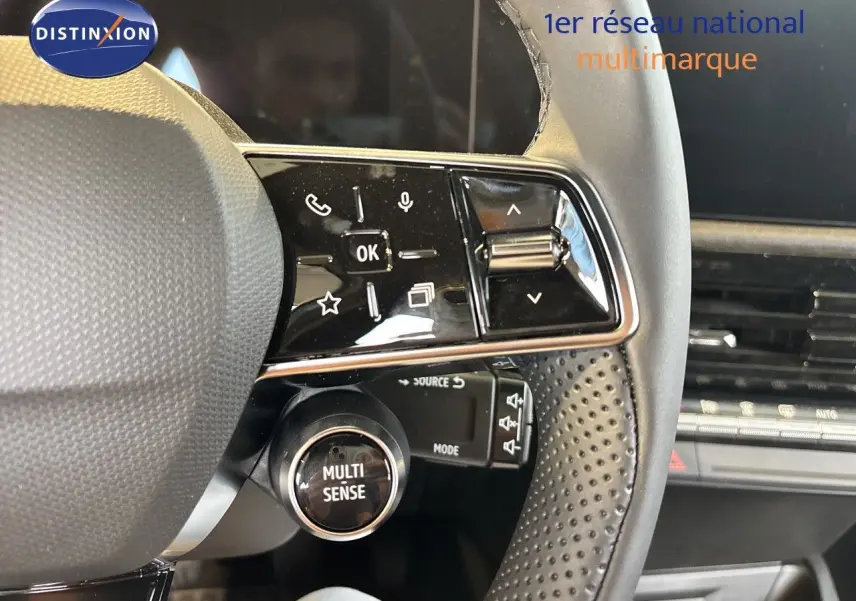 Gros plan sur le volant noir perforé de la Renault Clio blanc glacier, avec commandes multifonctions et bouton Multi Sense visible.