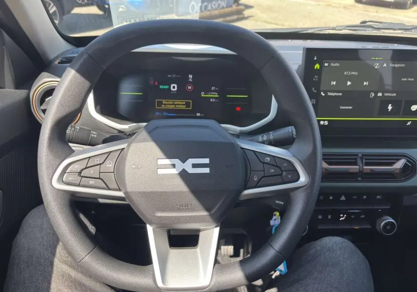 Vue intérieure centrée sur le volant DACIA Spring électrique avec tableau de bord numérique et écran tactile.
