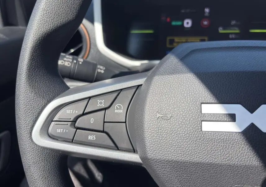Gros plan sur le volant avec commandes multifonctions du Dacia Spring électrique 65 Extrême, intérieur noir texturé.