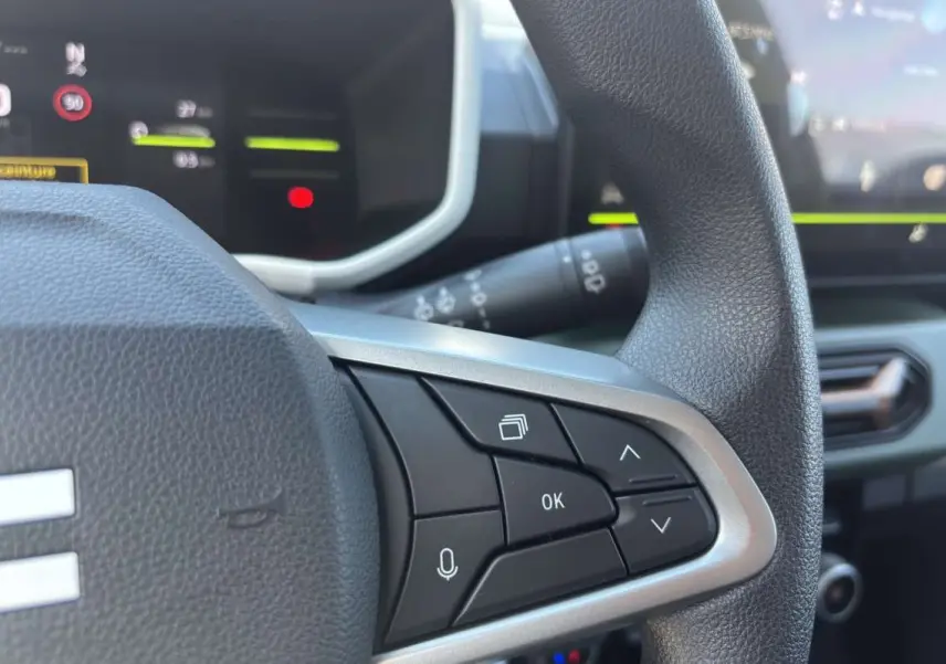 Gros plan sur les commandes au volant du Dacia Spring électrique 65 Extrême, intérieur moderne avec écran digital.