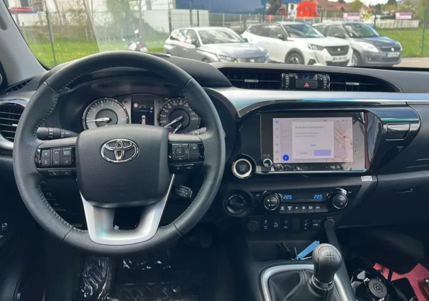 Intérieur du Toyota Hilux 2025 vert métal, vue du poste de conduite avec volant, tableau de bord et levier de vitesse manuel.