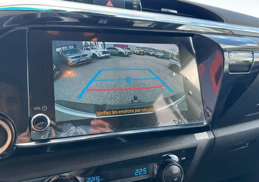 Vue arrière via caméra de recul du Toyota Hilux 4x4 vert métal 2025, avec lignes de guidage bleues et rouges à l'écran.