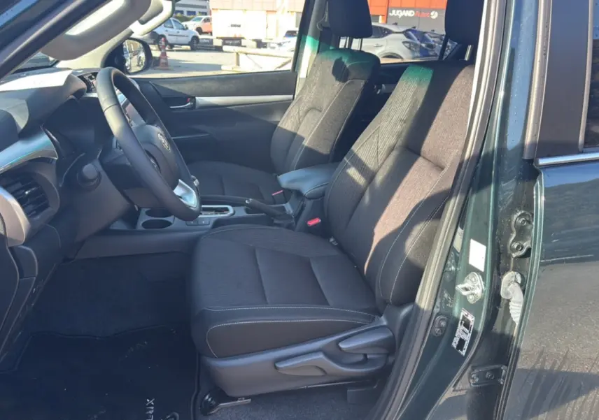 Vue intérieure côté conducteur du Toyota Hilux 2025 vert métal, montrant les sièges avant et le tableau de bord.