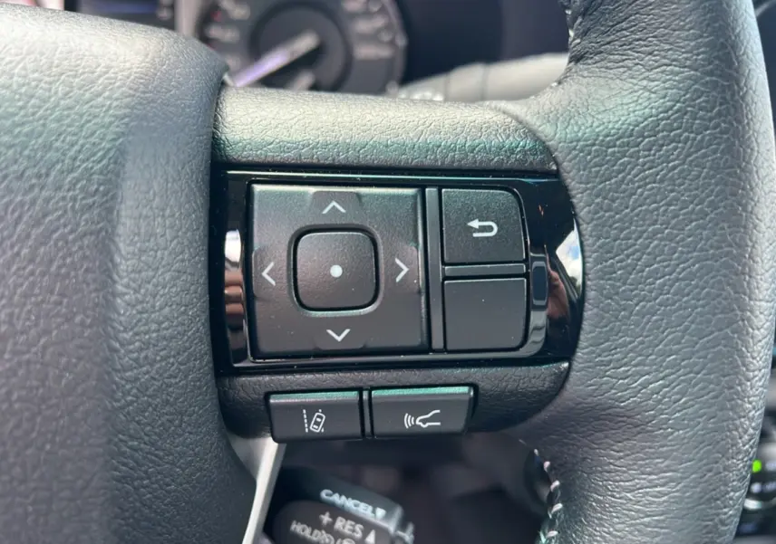 Gros plan sur les commandes multifonctions du volant en cuir noir du Toyota Hilux 4x4 vert métal 2025.