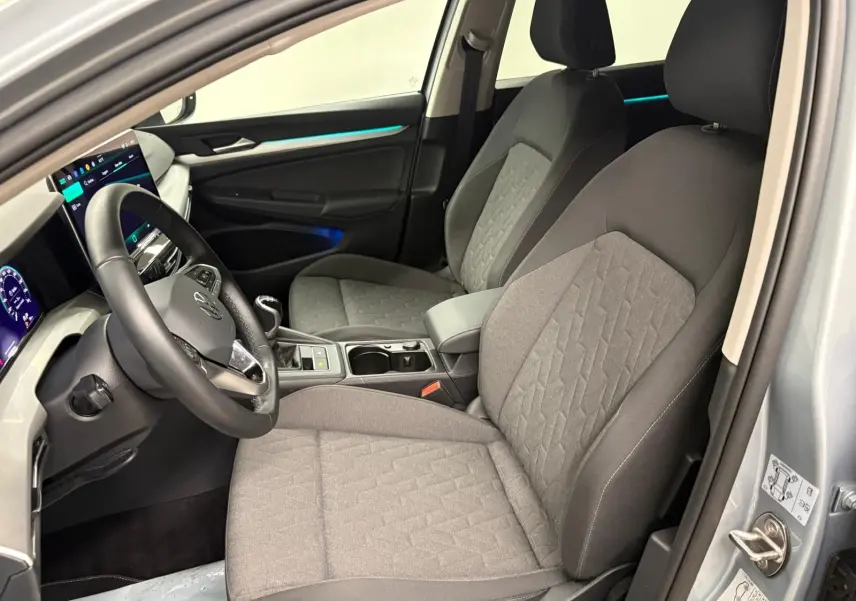 Vue intérieure côté conducteur de la Volkswagen Golf 1.5 TSI 2025 avec sièges tissu gris et éclairage d'ambiance bleu