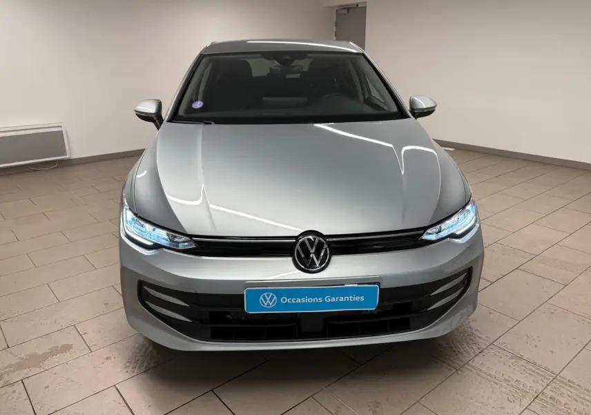 Vue avant d'une Volkswagen Golf 1.5 TSI 116 BVM6 VW Edition argent Dolomite avec phares LED allumés en intérieur.