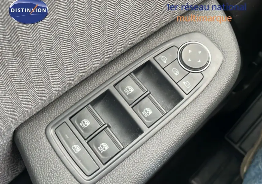 Gros plan sur les commandes de lève-vitres et rétroviseurs côté conducteur d'une Renault Clio gris schiste métal.