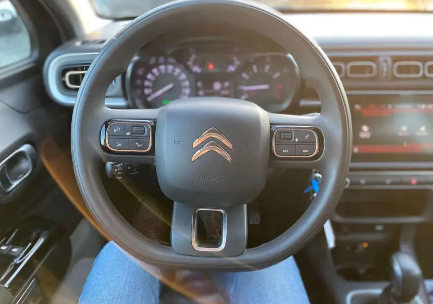 Vue centrée sur le volant du Citroën C3 Shine 2023, avec commandes audio intégrées et tableau de bord flou en arrière-plan.