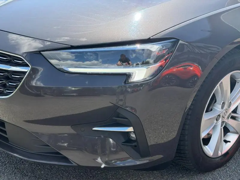 Gros plan sur le phare avant droit de l’Opel Insignia Grand Sport brun carbone avec jante alu visible.