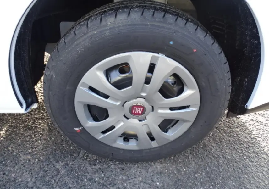 Gros plan sur la roue avant droite d’un Fiat Talento blanc avec enjoliveur gris et logo rouge FIAT.