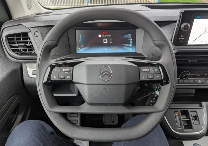 Vue intérieure centrée sur le volant carré noir et le combiné numérique du Citroën Jumpy XL 2025 gris.