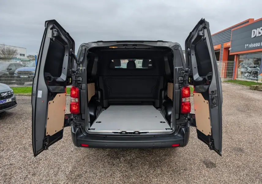 Vue arrière d'un Citroën Jumpy gris 2025 avec portes battantes ouvertes et plancher bois visible dans la zone de chargement.