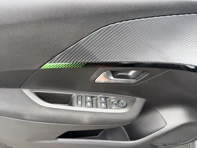 Détail de la porte côté conducteur de la Peugeot 208 gris foncé, avec commandes électriques et insert décor carbone.