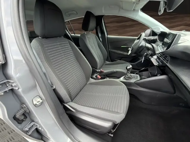 Intérieur avant de la Peugeot 208 gris foncé 2024, sièges tissu, volant cuir multifonctions et boîte manuelle visible.