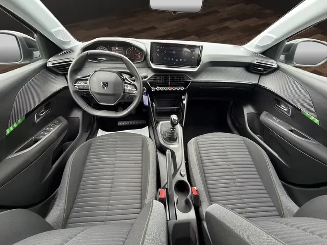 Vue intérieure avant de la Peugeot 208 100CH S&S Active 2024, volant cuir multifonctions et tableau de bord moderne gris foncé.