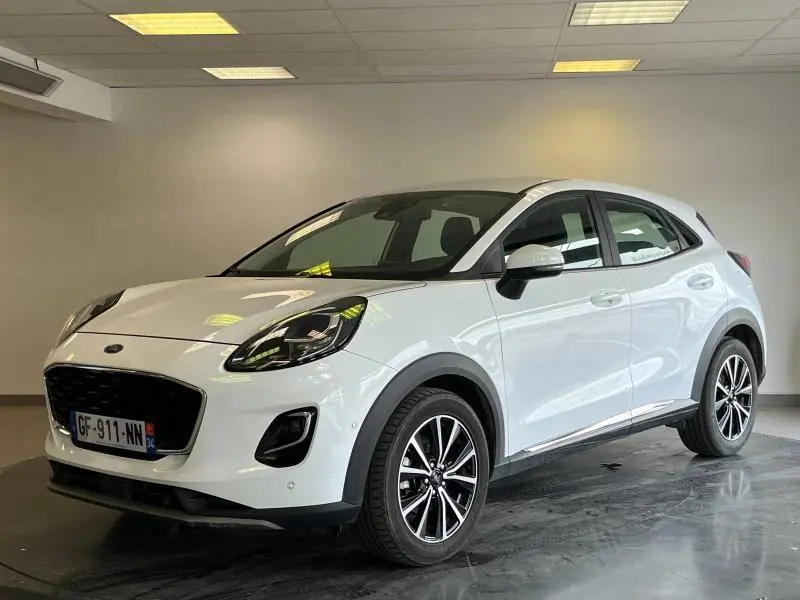 Ford Puma blanc glacier vu en 3/4 avant droit, avec jantes alliage et calandre noire dans un showroom.