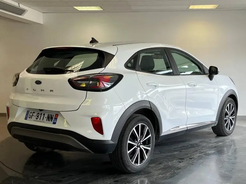 Vue 3/4 arrière droite du Ford Puma blanc glacier avec jantes alu et hayon électrique en intérieur showroom.
