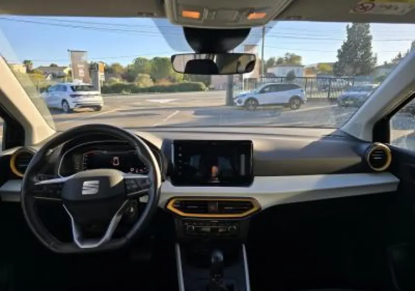 Vue intérieure avant du SEAT Arona 2024 avec tableau de bord clair, volant cuir multifonction et écran tactile central.