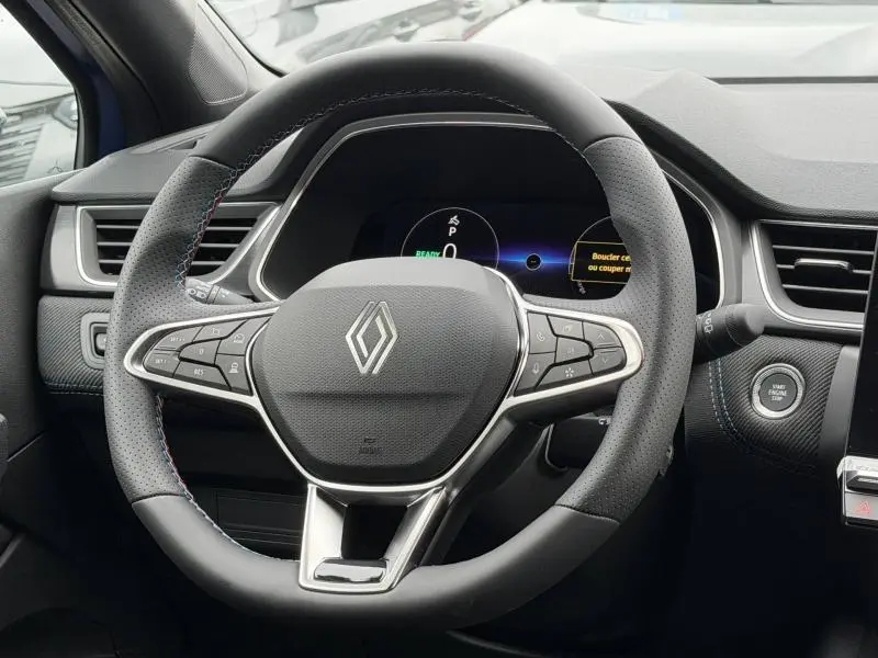 Vue rapprochée du volant perforé du Renault Captur 2026 hybride, avec coutures bleues et tableau de bord numérique.