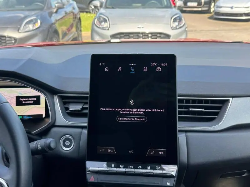Vue intérieure frontale du tableau de bord du Renault Captur rouge 2025, écran tactile central allumé.