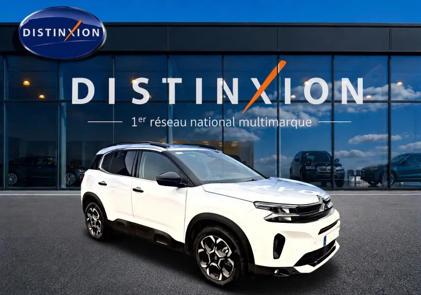 Citroën C5 Aircross blanc vue 3/4 avant droit, avec jantes alu noires et barres de toit visibles.