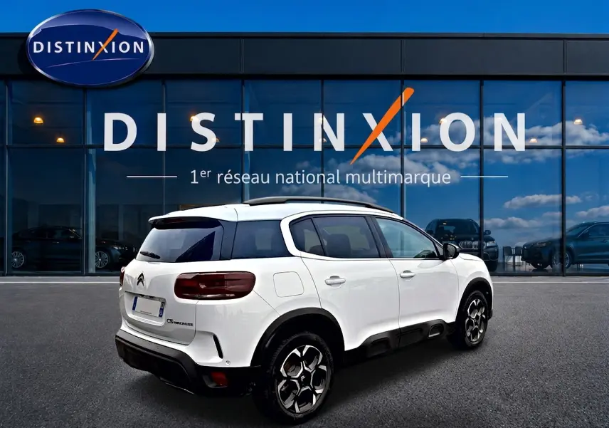 Vue 3/4 arrière droite d'un Citroën C5 Aircross blanc avec jantes alu et vitres arrière teintées, devant un bâtiment vitré.