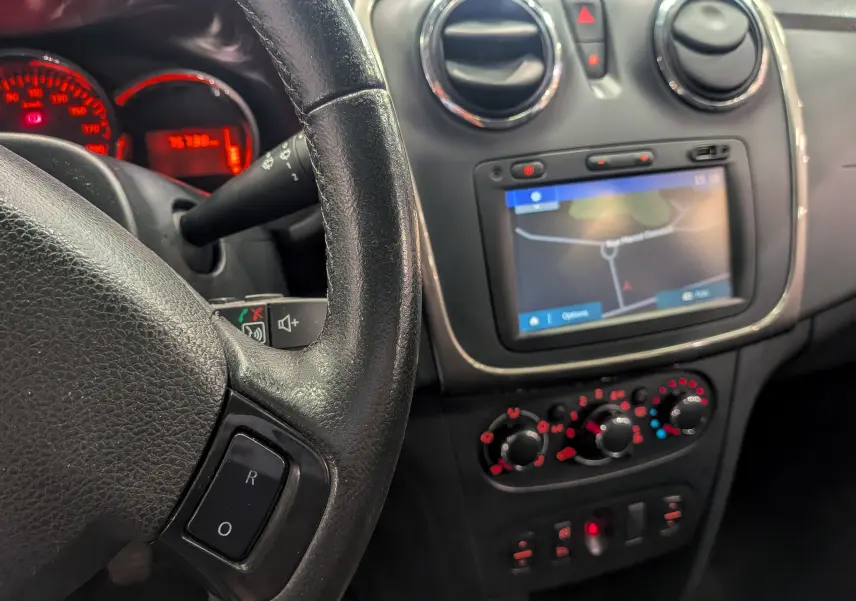 Intérieur de Dacia Sandero TCe 90 2015, vue sur le volant, tableau de bord et écran GPS tactile avec commandes climatiques.