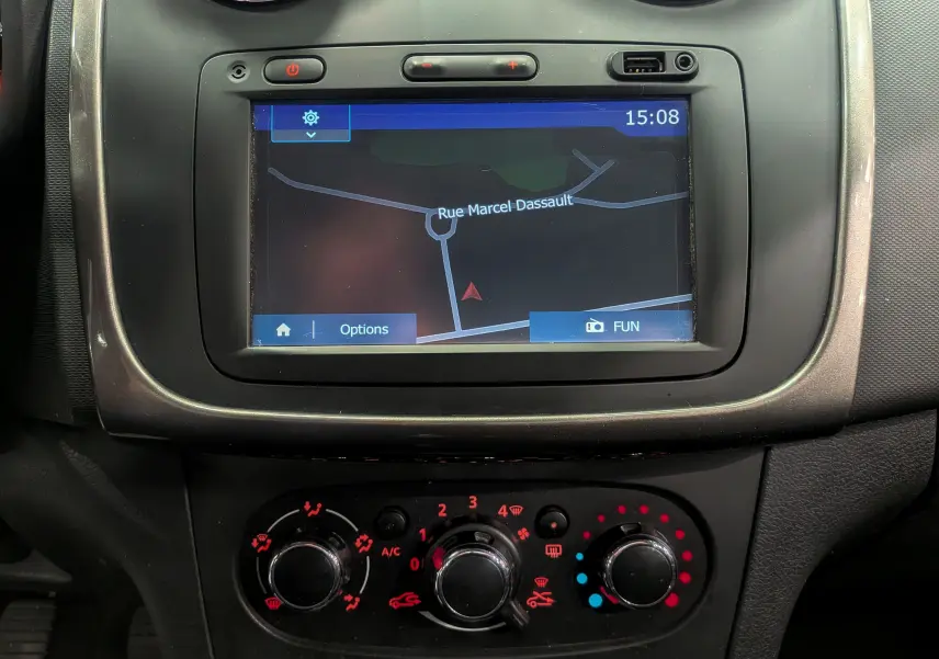 Écran tactile de navigation et commandes de climatisation rouges dans le tableau de bord d'une Dacia Sandero TCe 90 blanche de 2015.