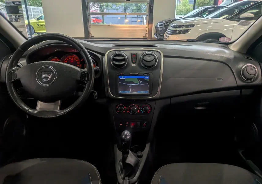 Intérieur de la Dacia Sandero TCe 90 2015 en vue frontale, tableau de bord noir avec écran GPS et volant cuir.