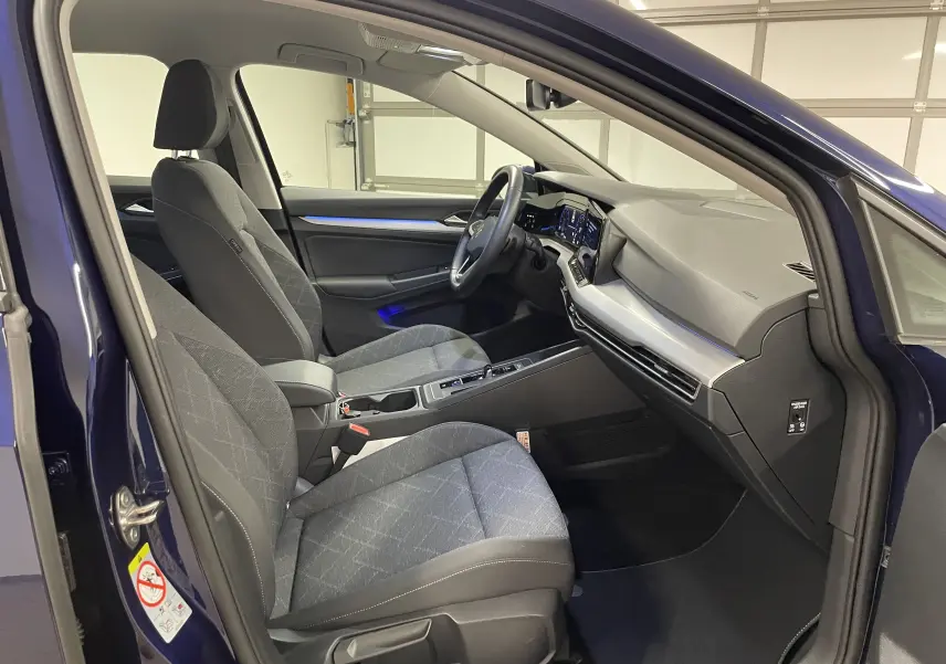 Intérieur côté conducteur d'une Volkswagen Golf 2023 bleu Atlantique, sièges tissu gris et tableau de bord moderne.