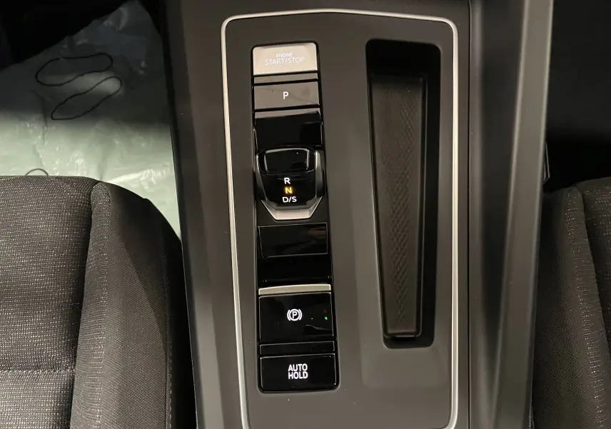 Console centrale noire avec levier de vitesses automatique et boutons start/stop, frein à main et auto hold dans une Volkswagen Golf 2023