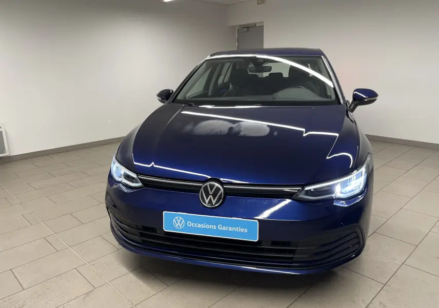 Volkswagen Golf 1.0 TSI 110 DSG7 Life Plus bleu Atlantique vue de face avec phares allumés en intérieur showroom.