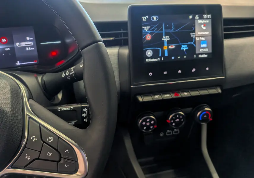 Vue intérieure rapprochée du tableau de bord et volant de la Renault Clio V gris Rafale avec écran tactile et commandes au volant.