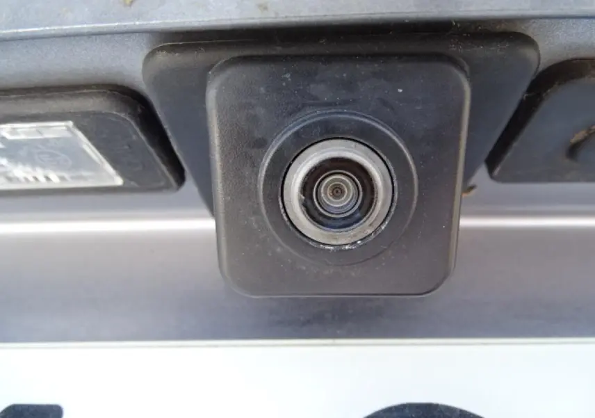 Gros plan sur la caméra de recul noire intégrée au hayon d’un Peugeot 3008 gris Artense, vue arrière.