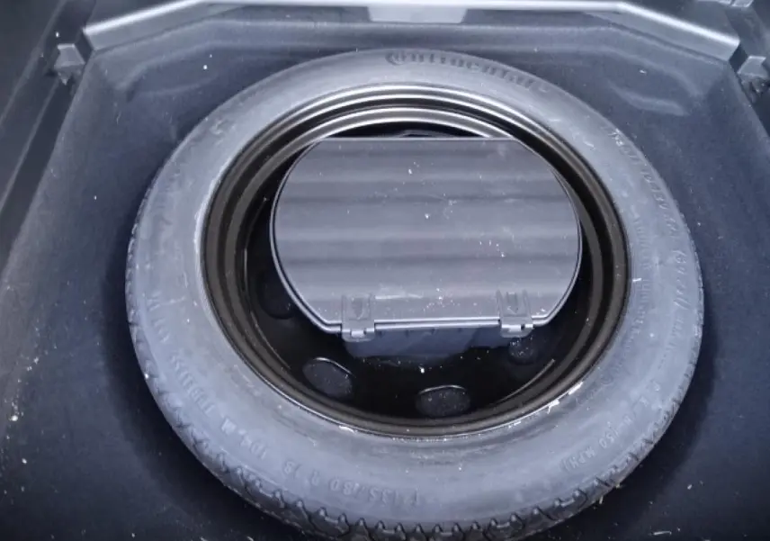 Gros plan sur la roue de secours galette noire dans le coffre du Peugeot 3008 gris Artense, vue de dessus.