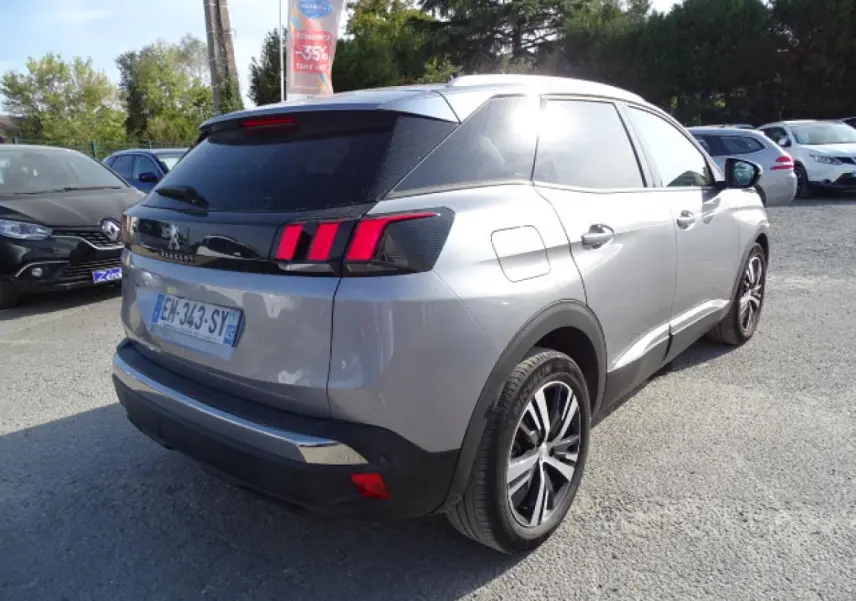 Vue 3/4 arrière droite d’un Peugeot 3008 gris Artense avec barres de toit en aluminium et feux arrière à griffes rouges.