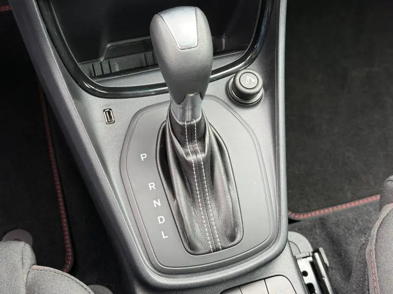 Gros plan sur le levier de vitesse automatique noir avec coutures blanches du Ford Puma 2024, console centrale et prise USB visibles.